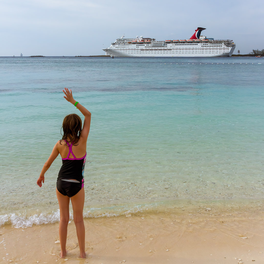 young girl standing in the water waving at cruise ship, Nassau