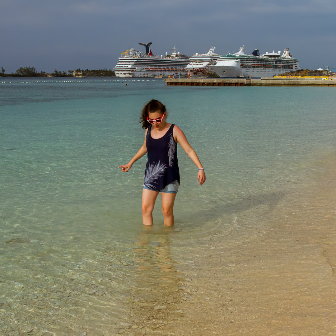 young girl standing in the water with cruise ships in the background, Nassau